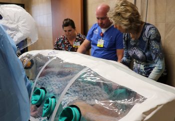 Gayla Tripp, Infection Prevention & Environmental Services Manager; Chad Garner, Director of Emergency and Trauma Services; and Rep. Kathy Swan look at the "patient" during the Ebola simulation training.