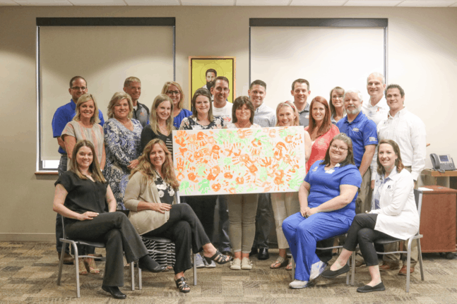Members of The Friends of Saint Francis and Jamie Jones, Jefferson Elementary Parent Liaison (center), pose with handprint artwork made by Jefferson Elementary students.