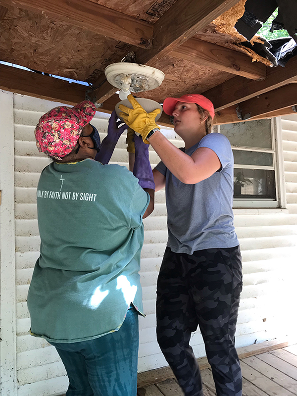 Rae Shaw-Johnson and volunteer Chrissy Wilferth remove a light fixture on the porch